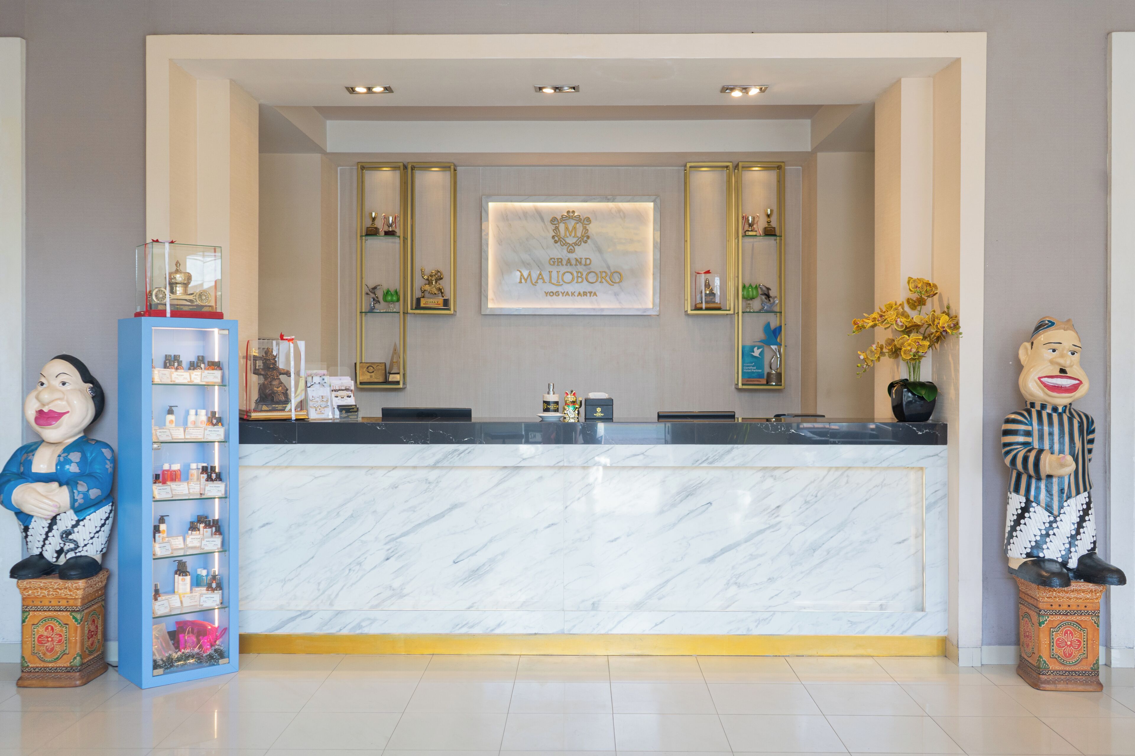 A reception desk with a marble counter, a framed logo, and decorative items including a statue and a shelf with bottles.