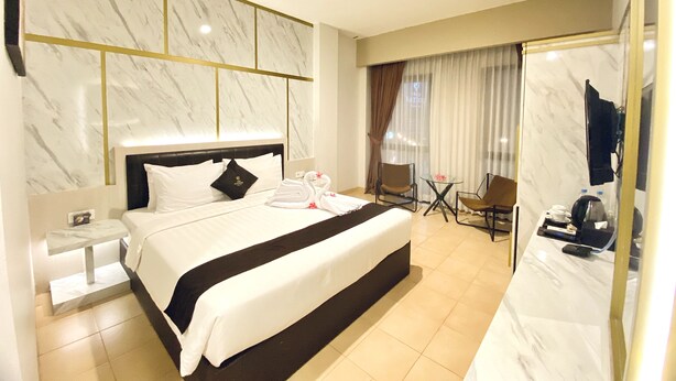 A hotel room with a large bed, a nightstand, a seating area with chairs, a table, and a mirror. - Grand Malioboro Hotel Yogyakarta (Yogyakarta)