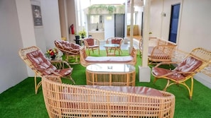 A room with wicker furniture, a glass table, and artificial grass flooring. - Grand Malioboro Hotel Yogyakarta (Yogyakarta)