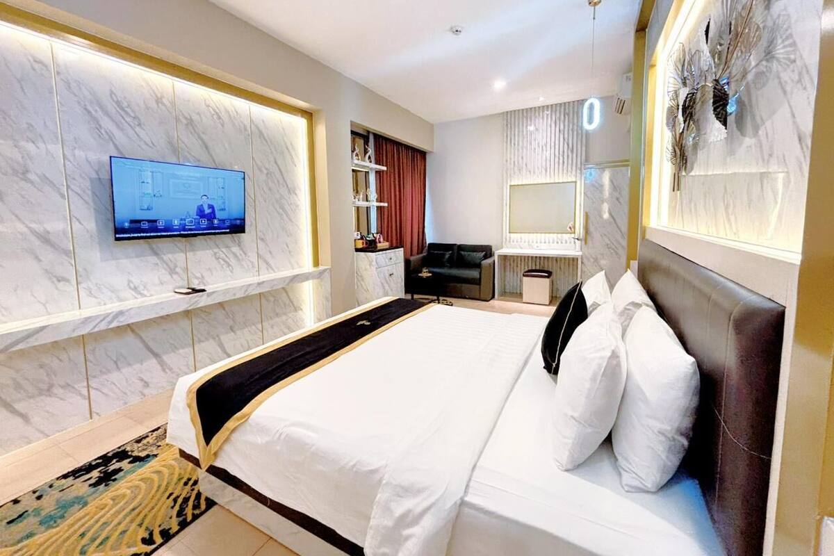 Ein modernes Hotelzimmer mit einem großen Bett, einem Flachbildfernseher an der Wand, einem Schreibtisch mit Stuhl und einem dekorativen Spiegel.