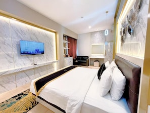 A modern hotel room with a large bed, a flat-screen TV mounted on the wall, a desk with a chair, and a decorative mirror. - Grand Malioboro Hotel Yogyakarta (Yogyakarta)