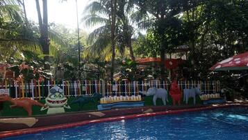 A swimming pool with a yellow and red poolside barrier, surrounded by lush greenery and various colorful animal sculptures.