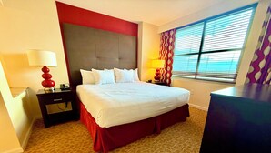 Ein Hotelzimmer mit einem großen Bett, zwei Nachttischen, einem Schreibtisch und einem Fenster mit Jalousien.