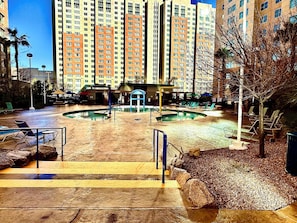 A hotel courtyard with a swimming pool, lounge chairs, and a building with multiple floors in the background. - 2-bedroom condo in terrific Las Vegas with AC and fitness room (Las Vegas)