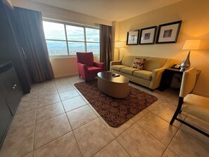 A living room with a sofa, armchair, coffee table, and a view of the city through large windows. - 2-bedroom condo in terrific Las Vegas with AC and fitness room (Las Vegas)