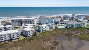 An aerial view of a coastal residential area with beachfront properties, a pier, and a swimming pool. - New! Coastal Condo - Pool with Marsh + Ocean Views (Carolina Beach)