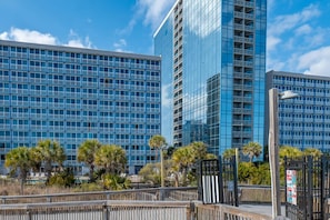 Ein modernes Hotel mit einer gläsernen Fassade, mehreren Balkonen und einer Holzpromenade im Vordergrund.