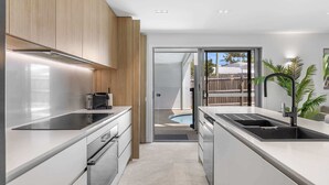 Une cuisine moderne dotée d’appareils électroménagers en acier inoxydable, de meubles en bois et offrant une vue sur un jardin avec piscine.