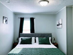 A bedroom with a bed, two nightstands, a window with curtains, and a ceiling light. - Indy-Themed Classic: Ode to Hoosier Spirit (Indianapolis)