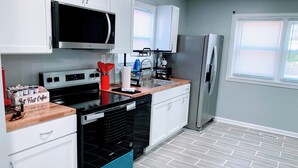 A modern kitchen with white cabinets, a stainless steel refrigerator, a microwave, and a dishwasher. - Indy-Themed Classic: Ode to Hoosier Spirit (Indianapolis)