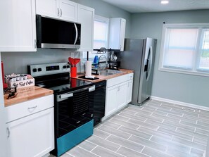 A modern kitchen with white cabinets, a stainless steel refrigerator, a microwave, and a dishwasher. - Indy-Themed Classic: Ode to Hoosier Spirit (Indianapolis)