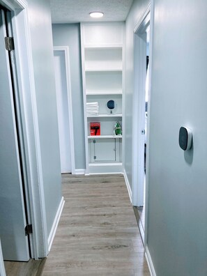 A hallway with white walls, a wooden floor, and a shelf with a mirror and a box. - Indy-Themed Classic: Ode to Hoosier Spirit (Indianapolis)