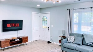A living room with a flat-screen TV displaying 'NETFLIX,' a wooden entertainment unit, a grey sofa, and a patterned rug. - Indy-Themed Classic: Ode to Hoosier Spirit (Indianapolis)