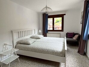 A bedroom with a bed, a window, a radiator, a bedside table, and a chair. - Casa Antonio en Picos de Europa (Inguanzo)
