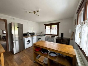 A compact kitchen with a refrigerator, washing machine, microwave, and wooden table with bowls. - Casa Antonio en Picos de Europa (Inguanzo)