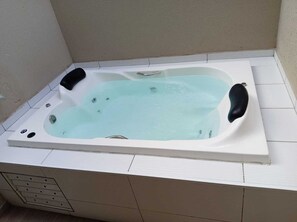 Ein rechteckiges Whirlbad mit hellblauem Innenraum, einem schwarzen Sitz und einem weiß gefliesten Boden.