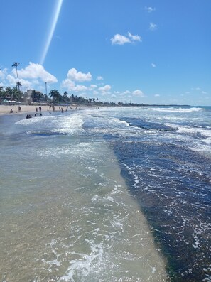 Ein Strand mit klarem Wasser, Palmen und einer entfernten Küstenlinie.