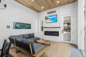 Ein Zimmer mit grauem Sofa, einem Holztisch, einem Fischgemälde, einem Fernseher und einem Kamin.