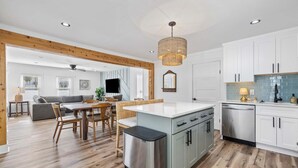 Una cucina moderna con mobili bianchi, una lavastoviglie in acciaio inossidabile e un'area pranzo con tavolo e sedie in legno.