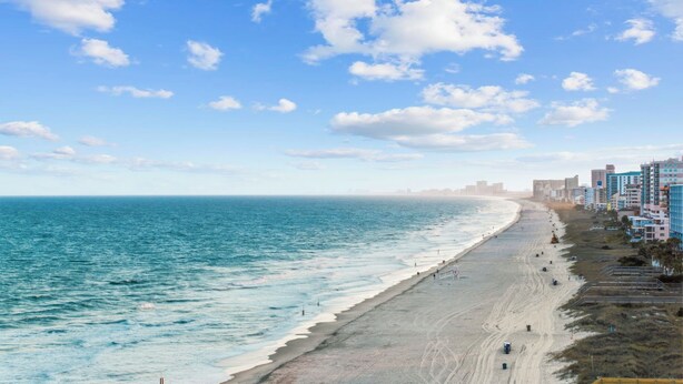 Una spiaggia con un'ampia distesa di sabbia, un mare azzurro cristallino e una fila di edifici lungo la riva.