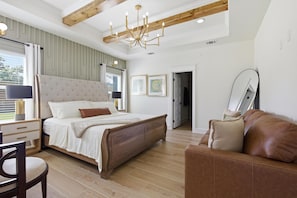 Une chambre à coucher comprenant un lit, une tête de lit en bois, une table de chevet, une chaise, un canapé, un lustre et un miroir.