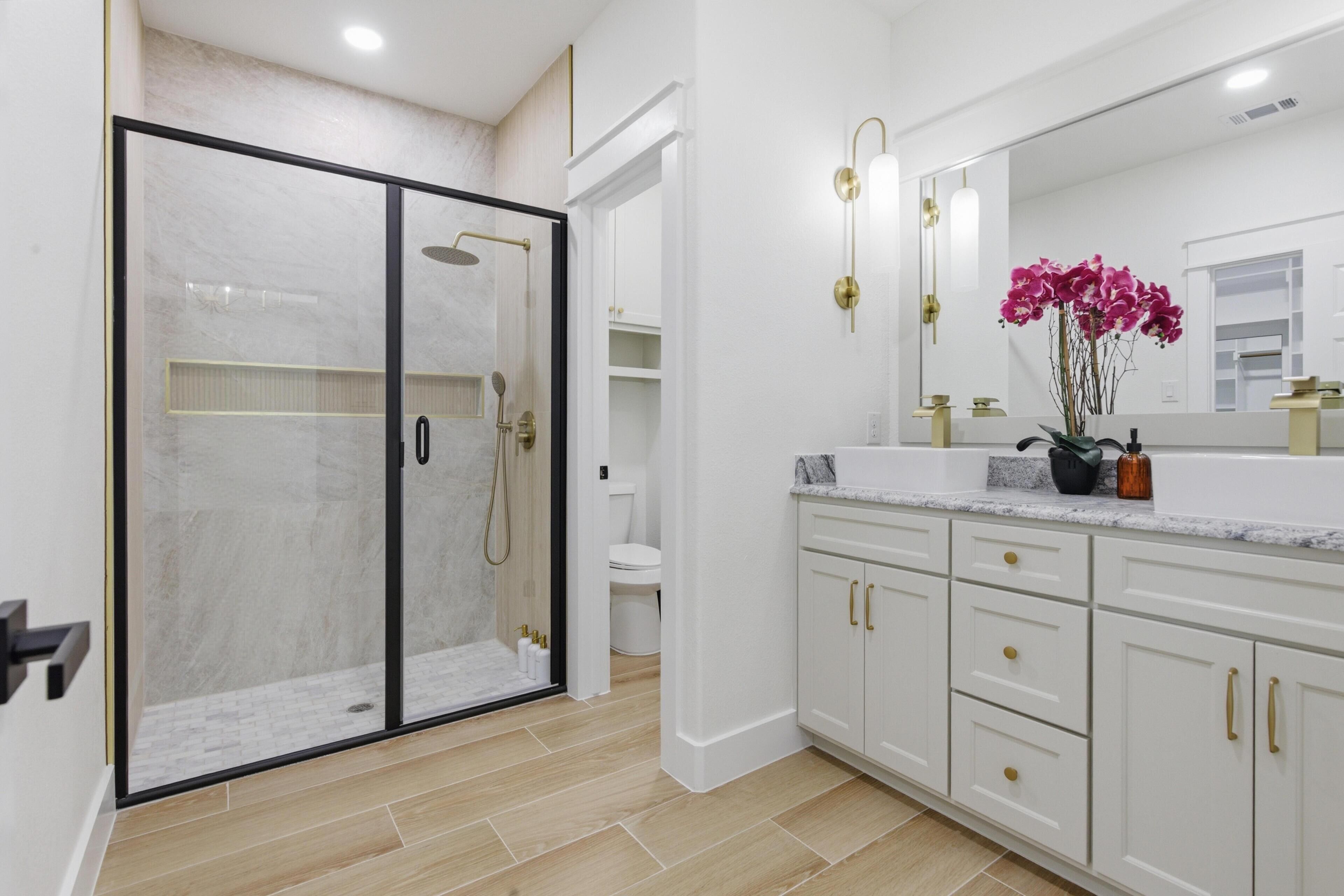 A modern bathroom with a glass shower enclosure, white cabinetry, and a large mirror.
