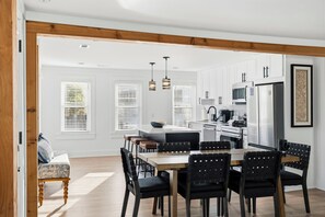 Una cucina moderna con mobili bianchi, un'area pranzo con tavolo di legno e sedie nere, e vista sul soggiorno adiacente.