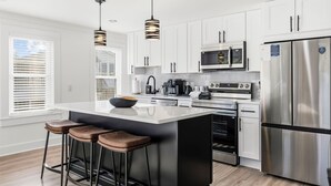A modern kitchen with white cabinets, stainless steel appliances, and a central island with stools. - Bijou House Unit 2 - 5BR w/ Ocean Views + Heated Pool & Hot Tub (Walk to Beach!) (North Myrtle Beach)