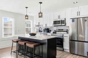Una cocina moderna con gabinetes blancos, electrodomésticos de acero inoxidable y una isla central con taburetes.