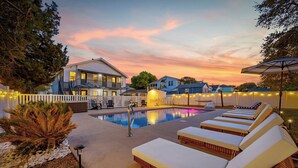 A swimming pool with lounge chairs, a white picket fence, and houses in the background. - Bijou House Unit 2 - 5BR w/ Ocean Views + Heated Pool & Hot Tub (Walk to Beach!) (North Myrtle Beach)