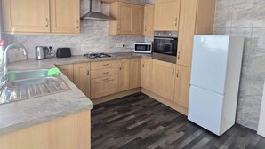 A compact kitchen with wooden cabinets, a gas stove, a microwave, and a refrigerator.