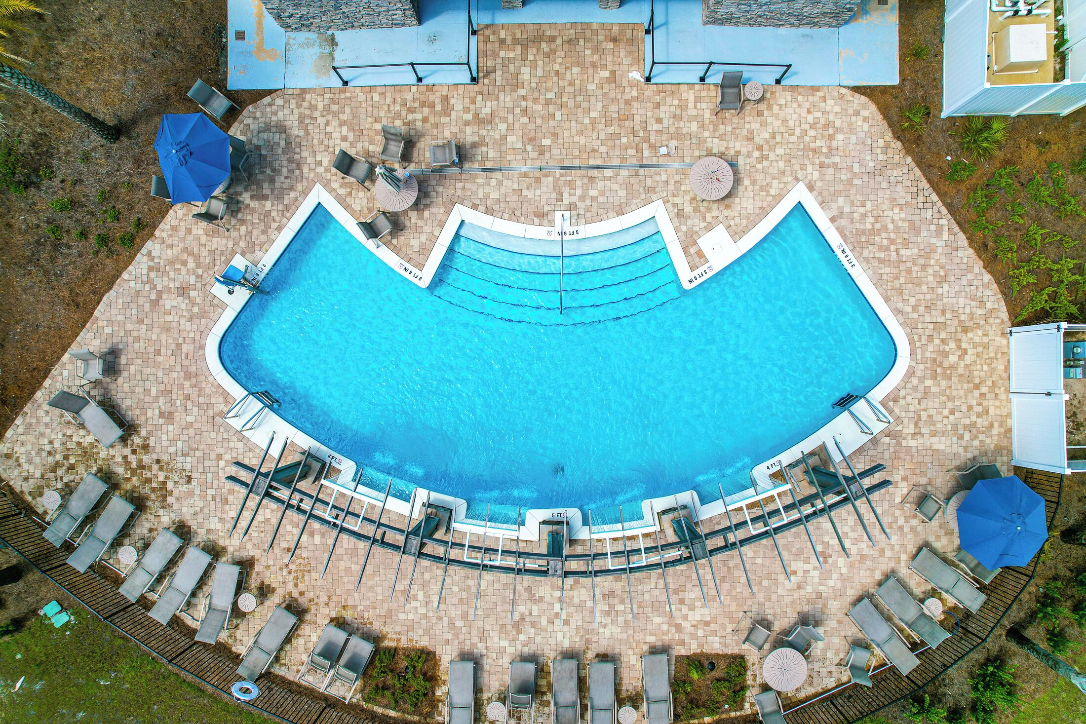 An aerial view of a swimming pool with lounge chairs and umbrellas, surrounded by a brick patio.
