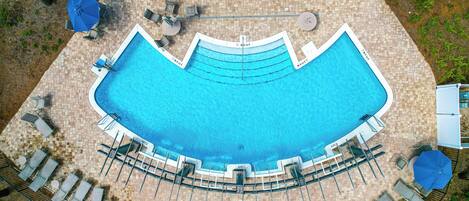 An aerial view of a swimming pool with lounge chairs and umbrellas, surrounded by a brick patio.