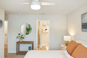 A bedroom with a bed, a nightstand, a lamp, a mirror, a wooden console table with a plant, and a door leading to a bathroom. - 3-bedroom townhome in lovely Panama City Beach with pool (Panama City Beach)