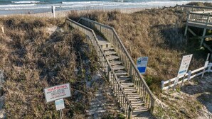 Eine Holztreppe führt zu einem Strandbereich, mit Warnschildern bezüglich Dünen und Bußgeldern bei unbefugtem Betreten.