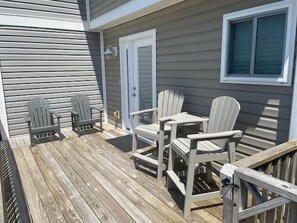 Une terrasse en bois avec des fauteuils Adirondack et une table, une porte et une fenêtre.