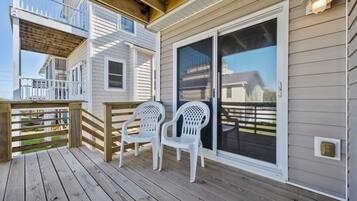 A wooden deck with two white plastic chairs, a wooden railing, and a sliding glass door.