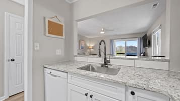 A kitchen with granite countertops, a stainless steel sink, white cabinetry, a ceiling fan, and a window with a view.