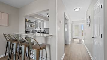 A modern kitchen with a bar area, a dining set, and a hallway leading to a door.