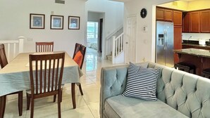 Un coin repas avec une table et des chaises, un canapé agrémenté d’un coussin à motifs, une cuisine avec des meubles en bois et un escalier menant à un autre niveau.