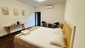 Una habitación de hotel con una cama, una mesita, sillas y cuadros en las paredes.