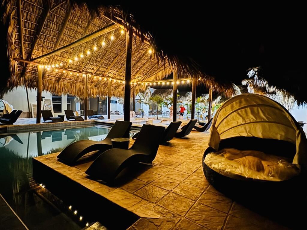 Zona de piscina con sillones de descanso, una estructura de techo de paja y vista despejada a la piscina.