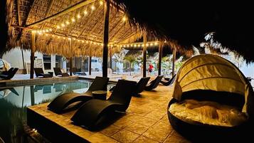 Zona de piscina con sillones de descanso, una estructura de techo de paja y vista despejada a la piscina.