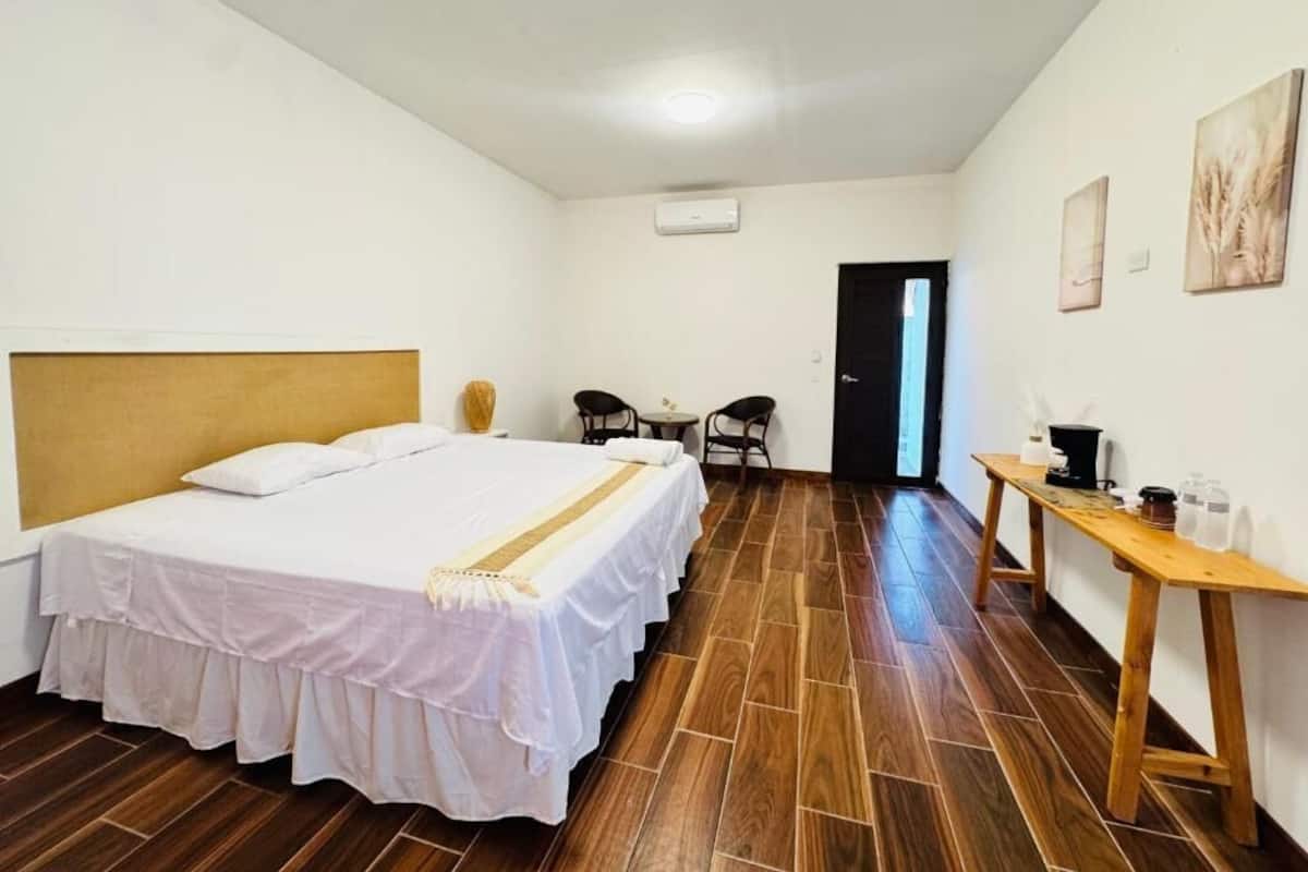 A bedroom with a bed, a wooden desk, two chairs, and a door.