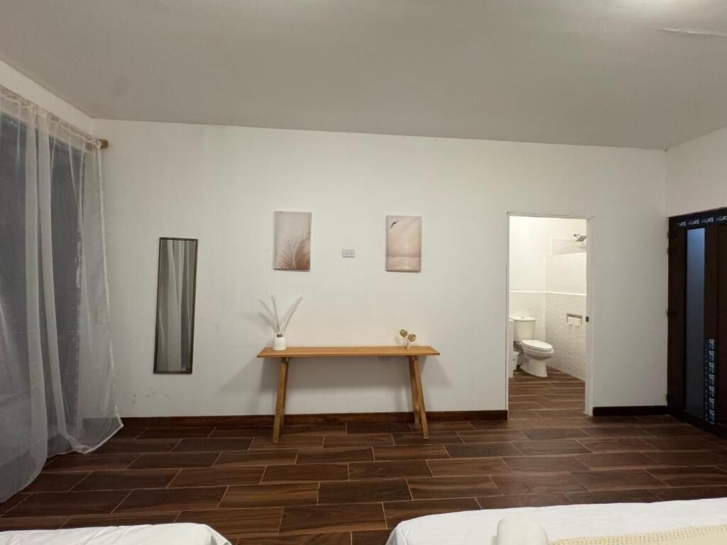Habitación de hotel con piso de madera, una cama, una mesita de noche con un florero y vista al baño.