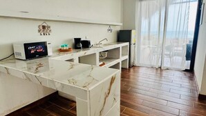 Una cocina con encimera de mármol, microondas, cafetera y lavabo. Hay un balcón con vistas.