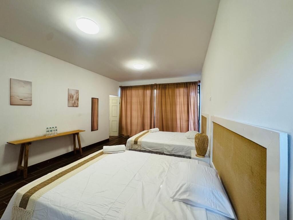 Une chambre d’hôtel avec deux lits, un banc en bois, une petite table et un vase fixé au mur.