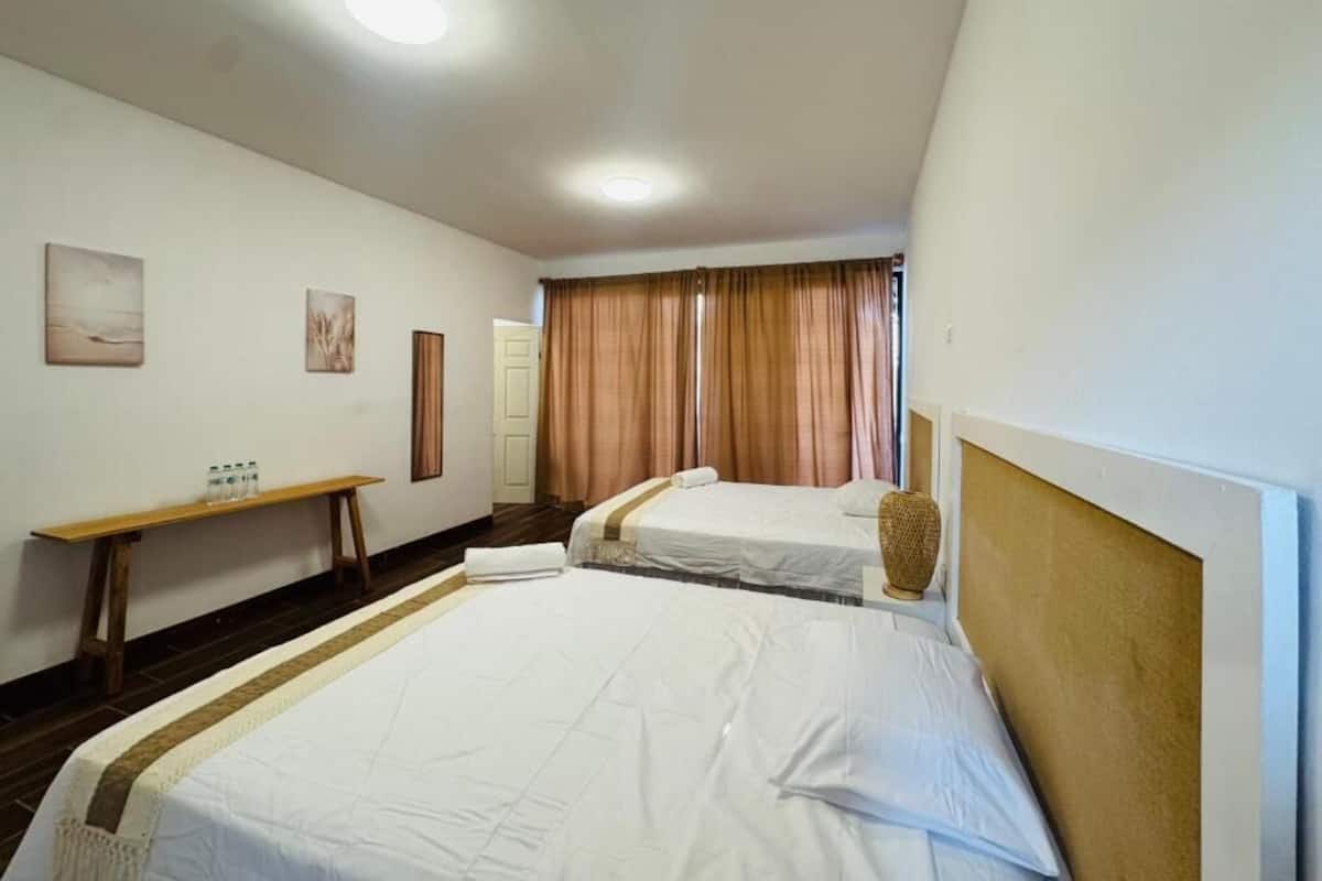 A hotel room with two beds, a wooden bench, a small table, and a wall-mounted vase.