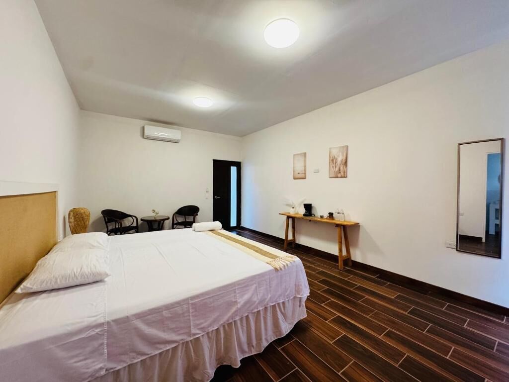 A hotel room with a bed, a small table with a lamp, a chair, and a wall-mounted mirror.