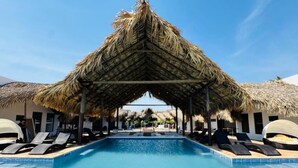 Una piscina con sillas de descanso, una estructura de techo de paja y un cielo azul despejado.